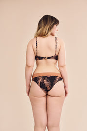Modelo plus size vestindo conjunto de biquíni com estampa botânica em fundo preto, vista traseira.