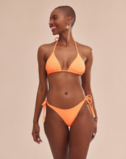 Imagem de um top de biquíni laranja com detalhes de amarração e ponteiras douradas, mostrado em um modelo.