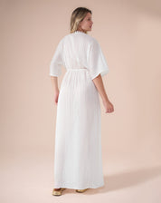 Vestido longo branco com mangas soltas e decote V, amarração abaixo do busto e fendas laterais, visto de costas.