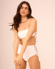 Top de biquíni off-white com design faixa e entrelaçados laterais, visto de lado.