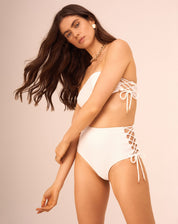 Top de biquíni off-white com design faixa e entrelaçados laterais, visto de frente em detalhe.