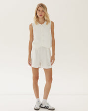 Modelo vestindo shorts de alfaiataria off-white com barra dobrada, vista frontal.