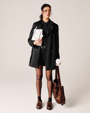 Modelo vestindo shorts curto reto de alfaiataria preto com camisa e blazer, segurando livros e bolsa.