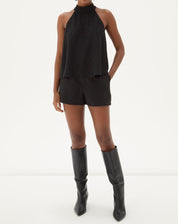 Modelo vestindo shorts curto reto de alfaiataria preto com blusa sem mangas e botas.