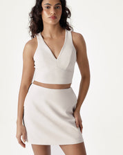 Modelo vestindo saia curta slim de alfaiataria bege com top branco, vista frontal.