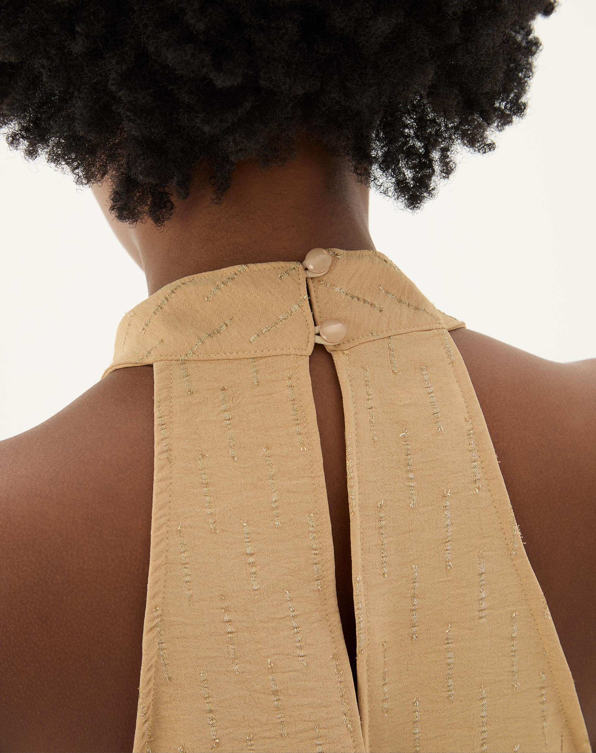 Fechamento traseiro da blusa frente única areia com botão.