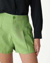 Close-up do shorts verde com vincos, mostrando detalhes do cós e botão.
