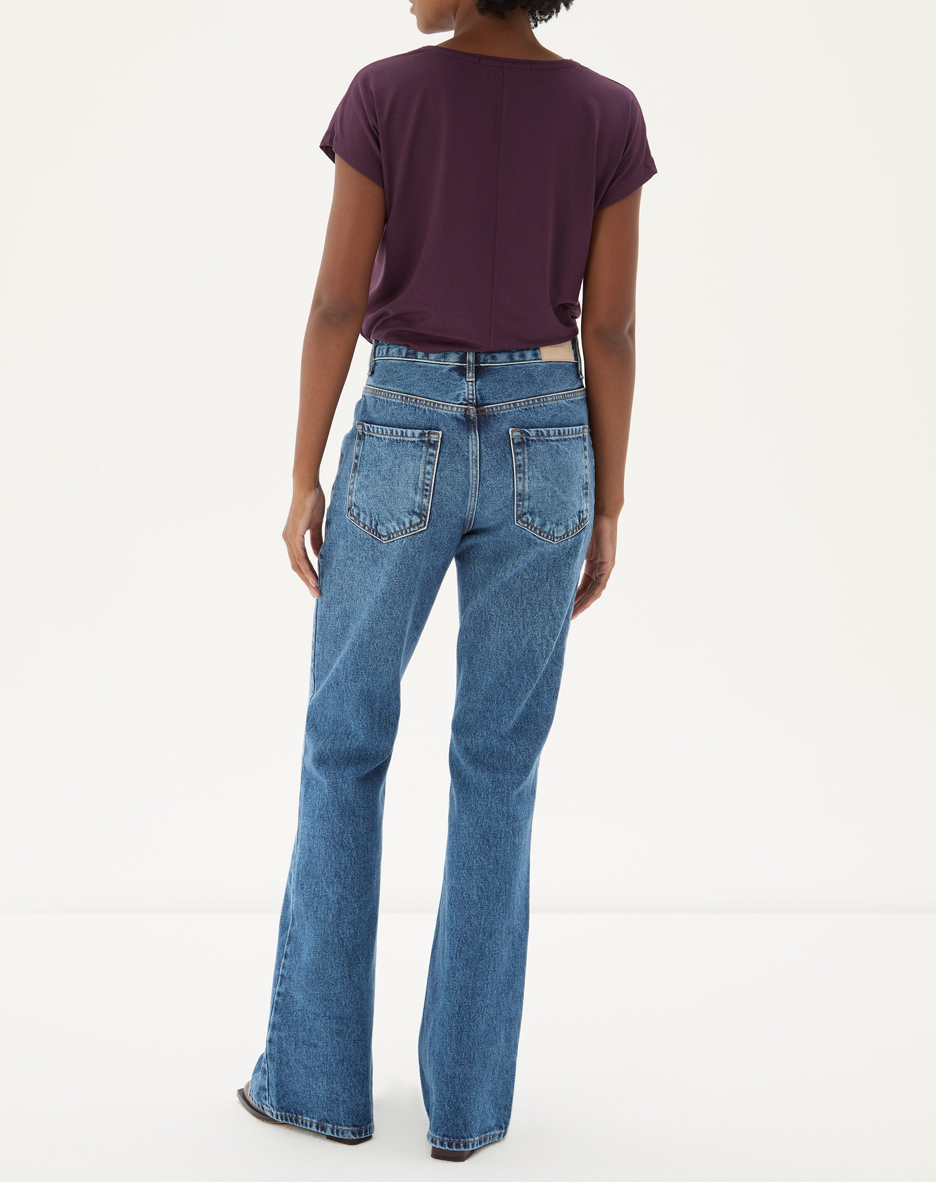 Vista traseira da calça jeans flare azul médio com blusa roxa.
