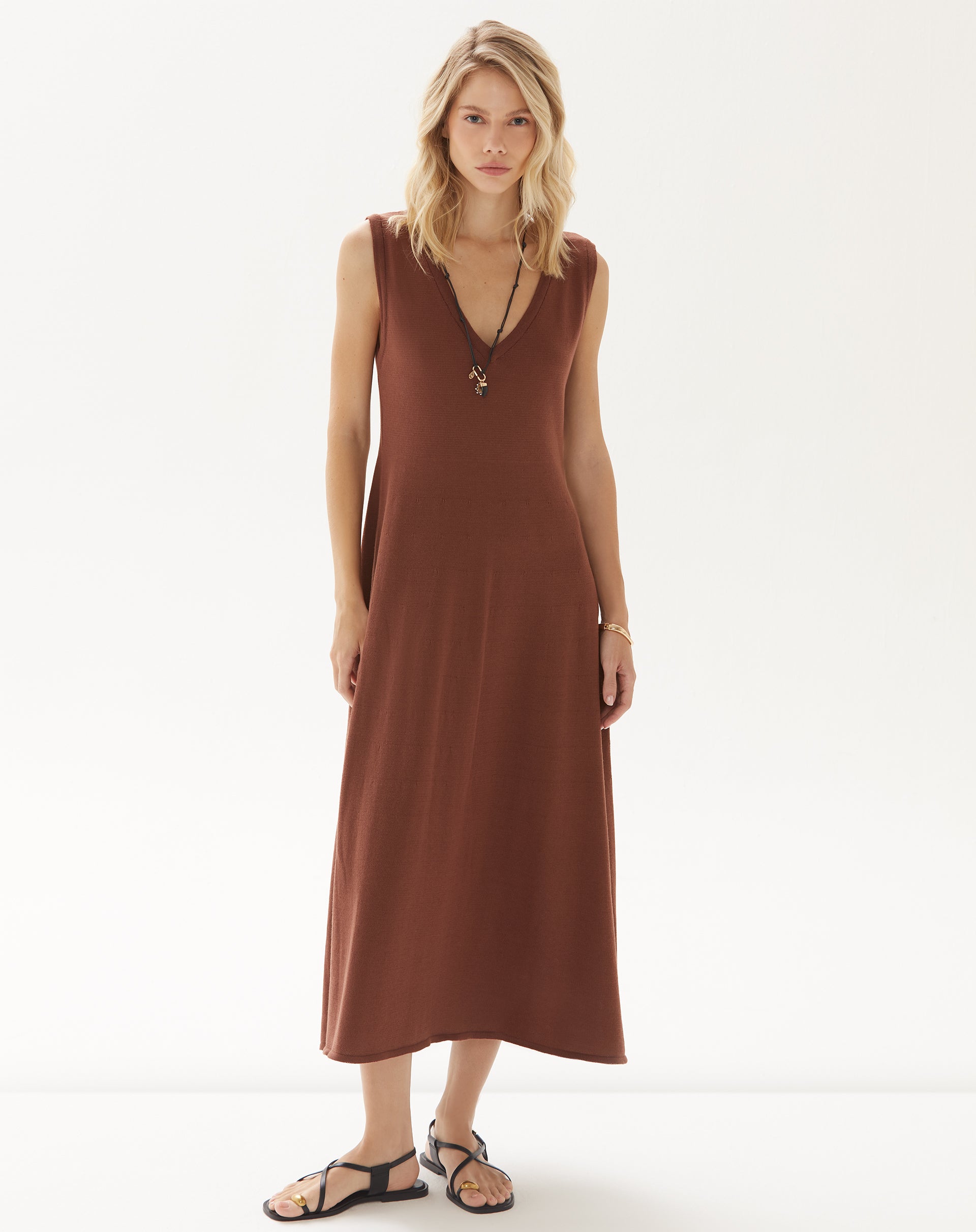 Imagem de uma modelo vestindo um vestido midi de tricot marrom, com decote em V e alças largas, em um fundo branco.