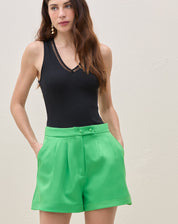 Detalhe frontal do shorts de alfaiataria verde com botões na cintura.