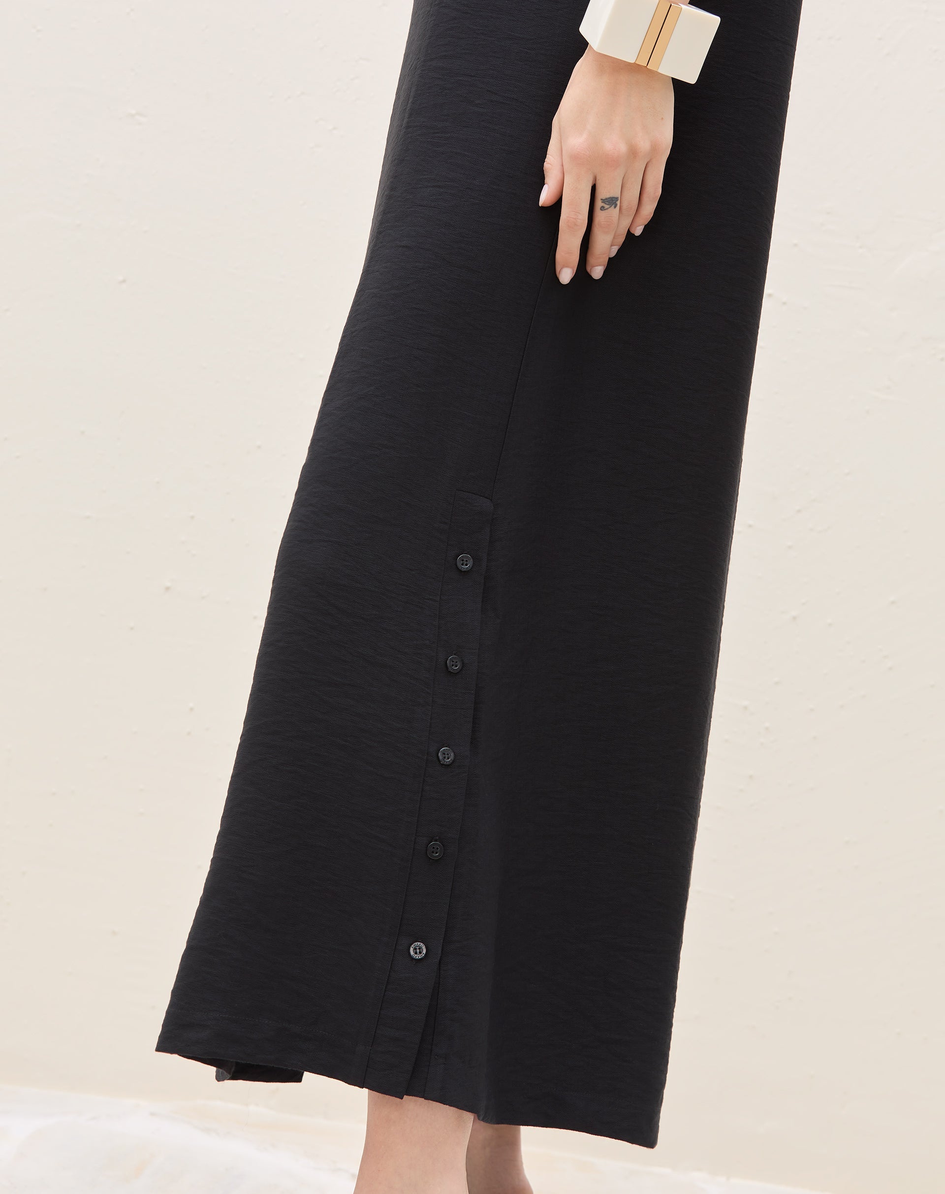 Detalhe do fechamento lateral com botões do vestido longo preto.
