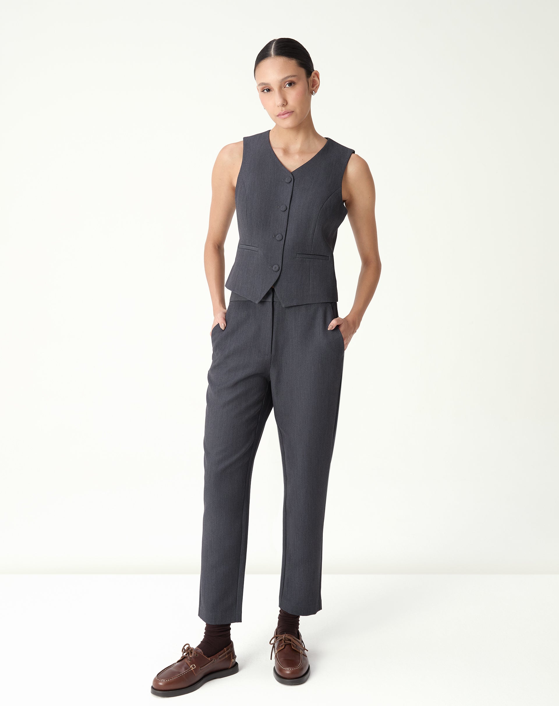 Modelo usa conjunto feminino com colete slim cinza e calça alfaiataria em fundo branco.