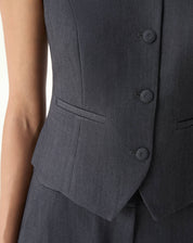 Detalhe do bolso embutido e dos botões forrados do colete alfaiataria cinza com acabamento visível.