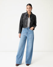 Vista completa da modelo usando jaqueta de couro preta curta com jeans de lavagem clara, look urbano e moderno