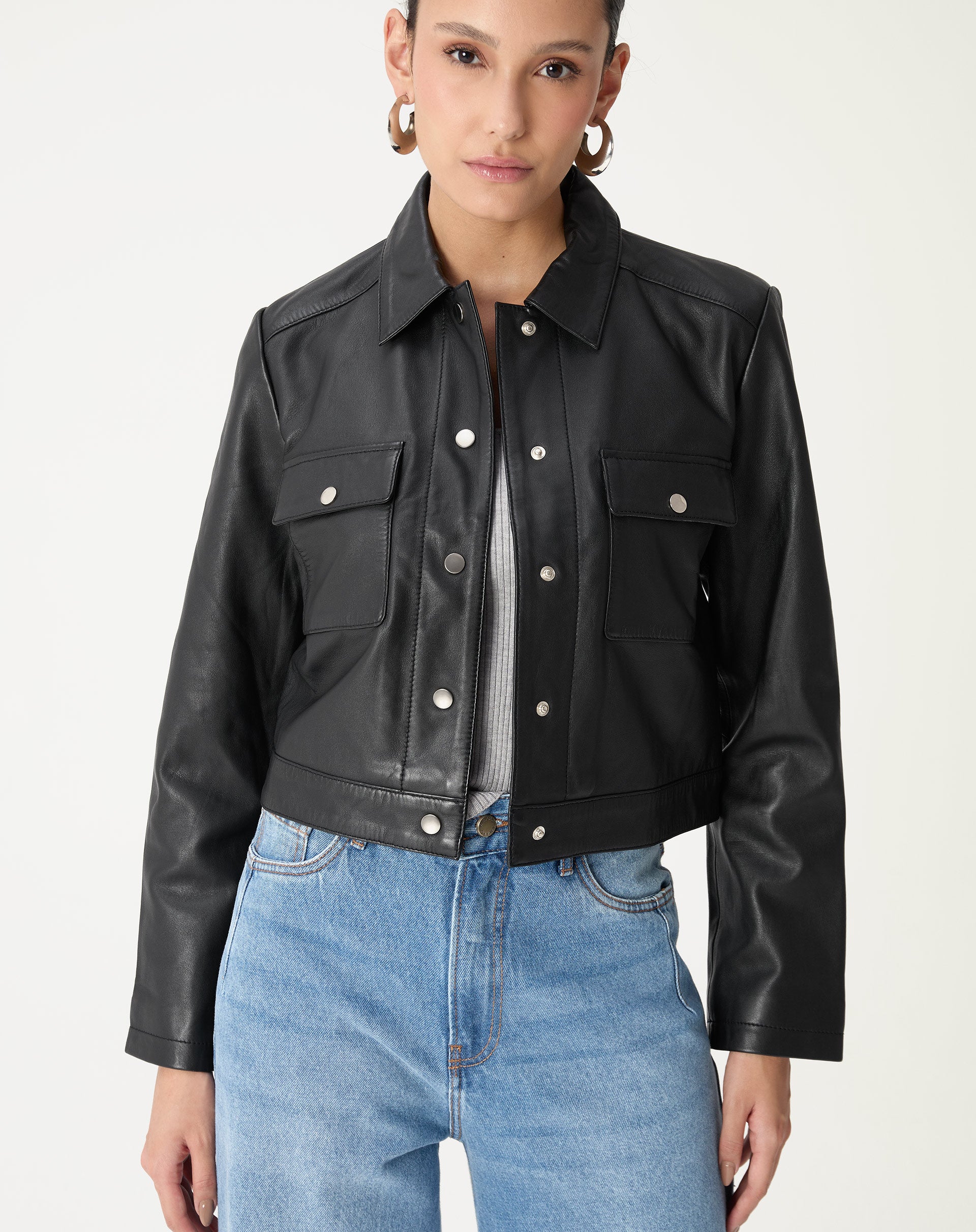 Visão frontal em modelo destacando os dois bolsos de aba com botões prateados e o corte reto da jaqueta preta