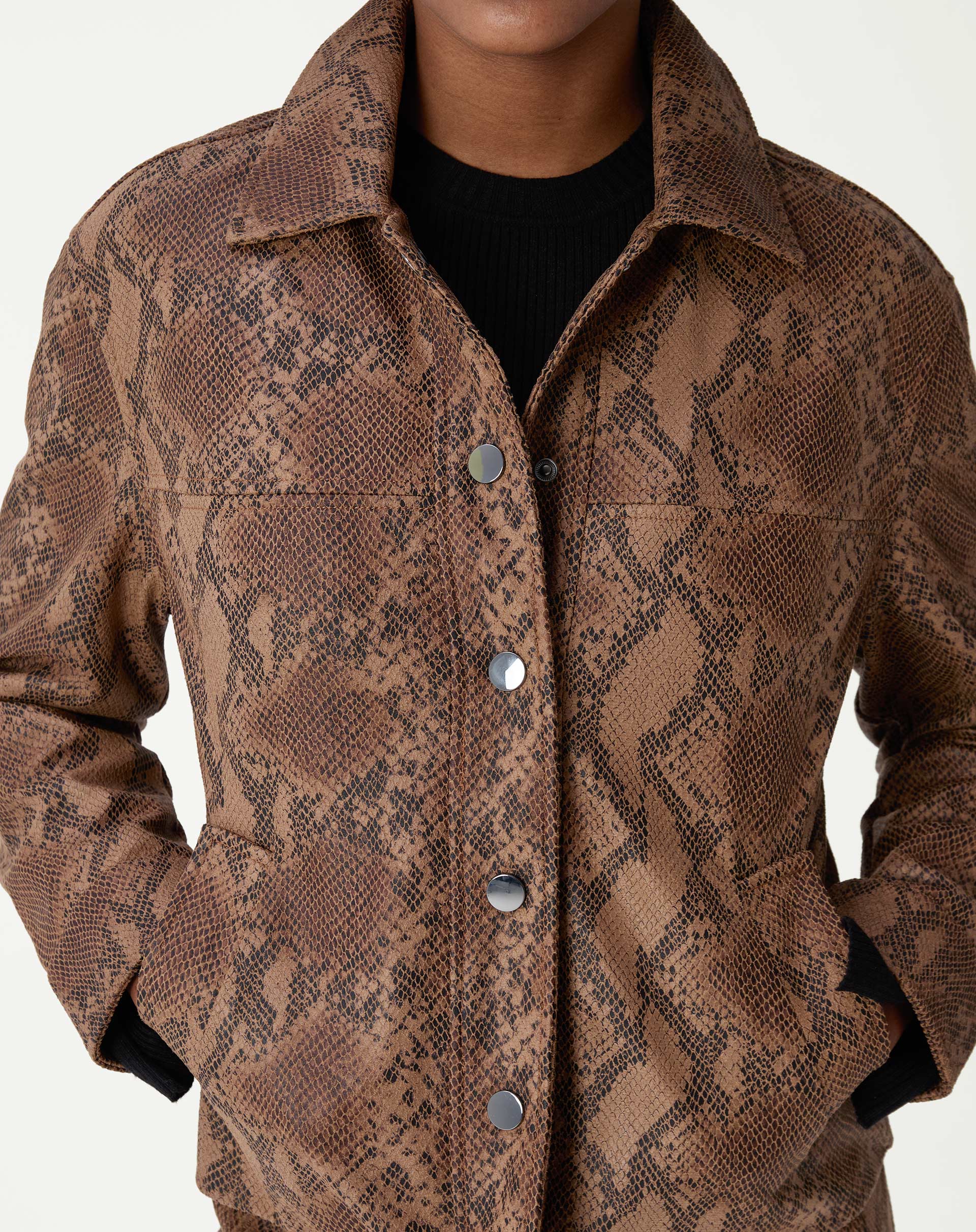 Detalhe frontal da jaqueta com mãos nos bolsos, fechamento por botões de pressão e textura animal print caramelo