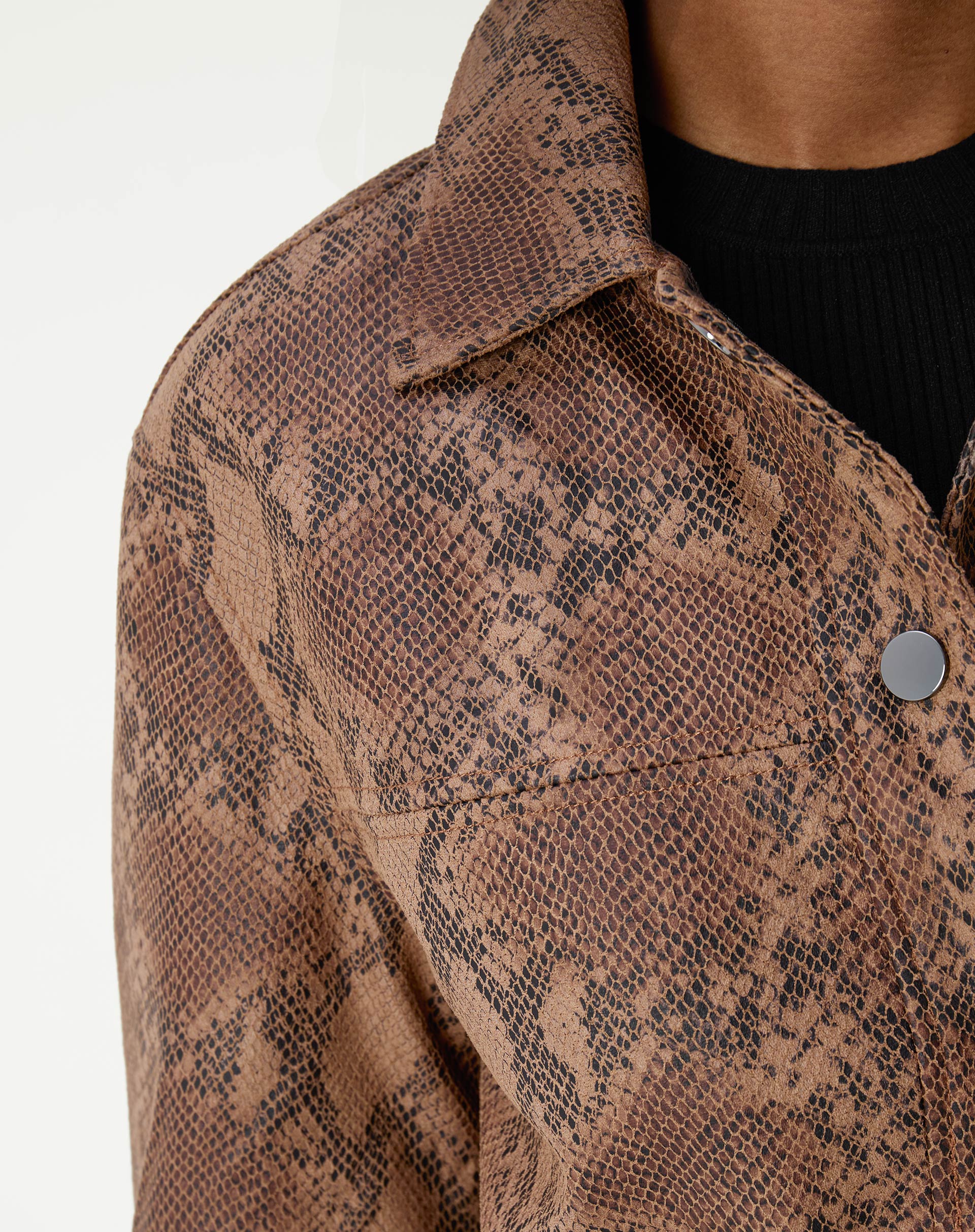 Close-up da gola e ombro da jaqueta em couro PU com estampa cobra caramelo mostrando textura de escamas e botão prateado