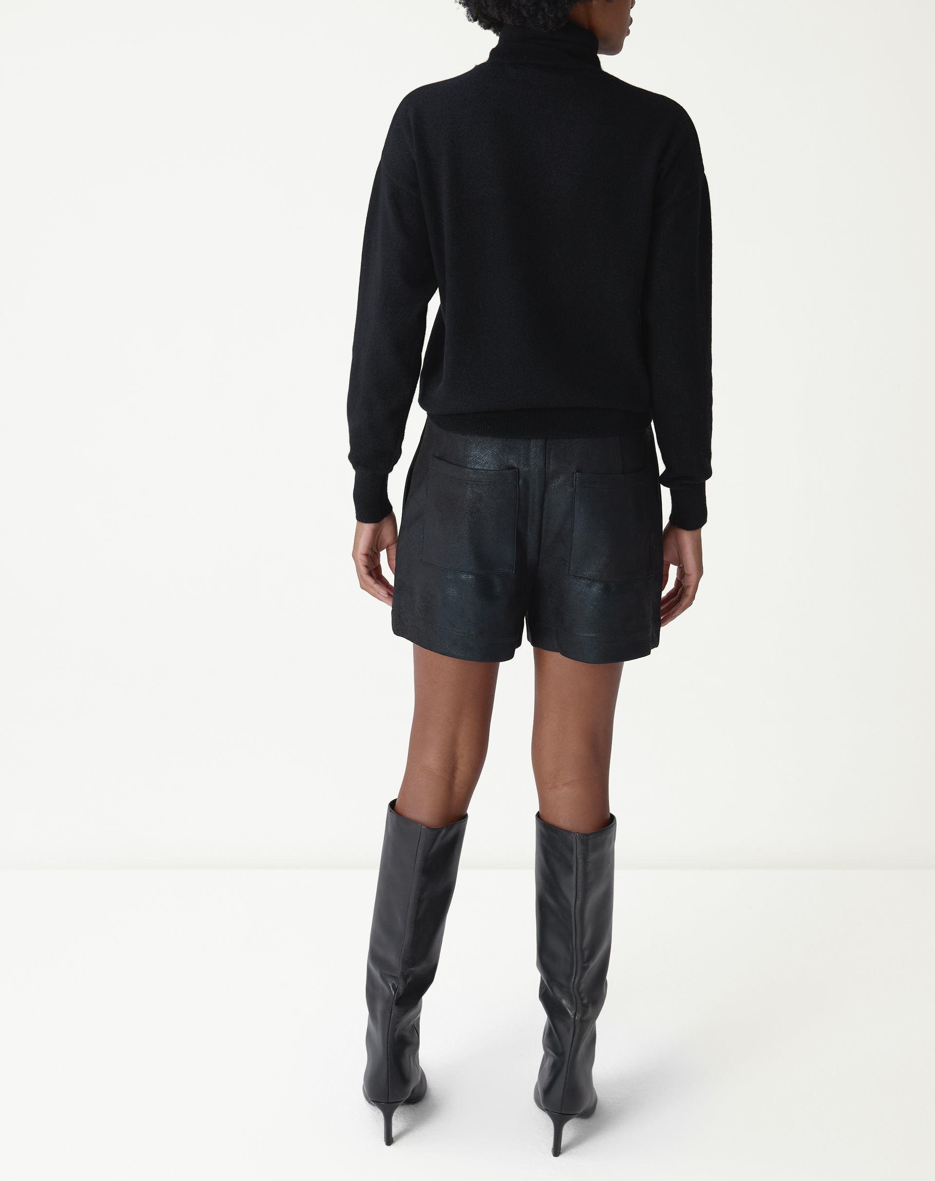 Vista de corpo inteiro frontal: shorts curto metalizado preto com suéter preto e botas de cano alto pretas, look moderno