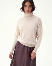 Modelo usando suéter cashmere areia em look com saia midi de couro, visão 3/4 frontal