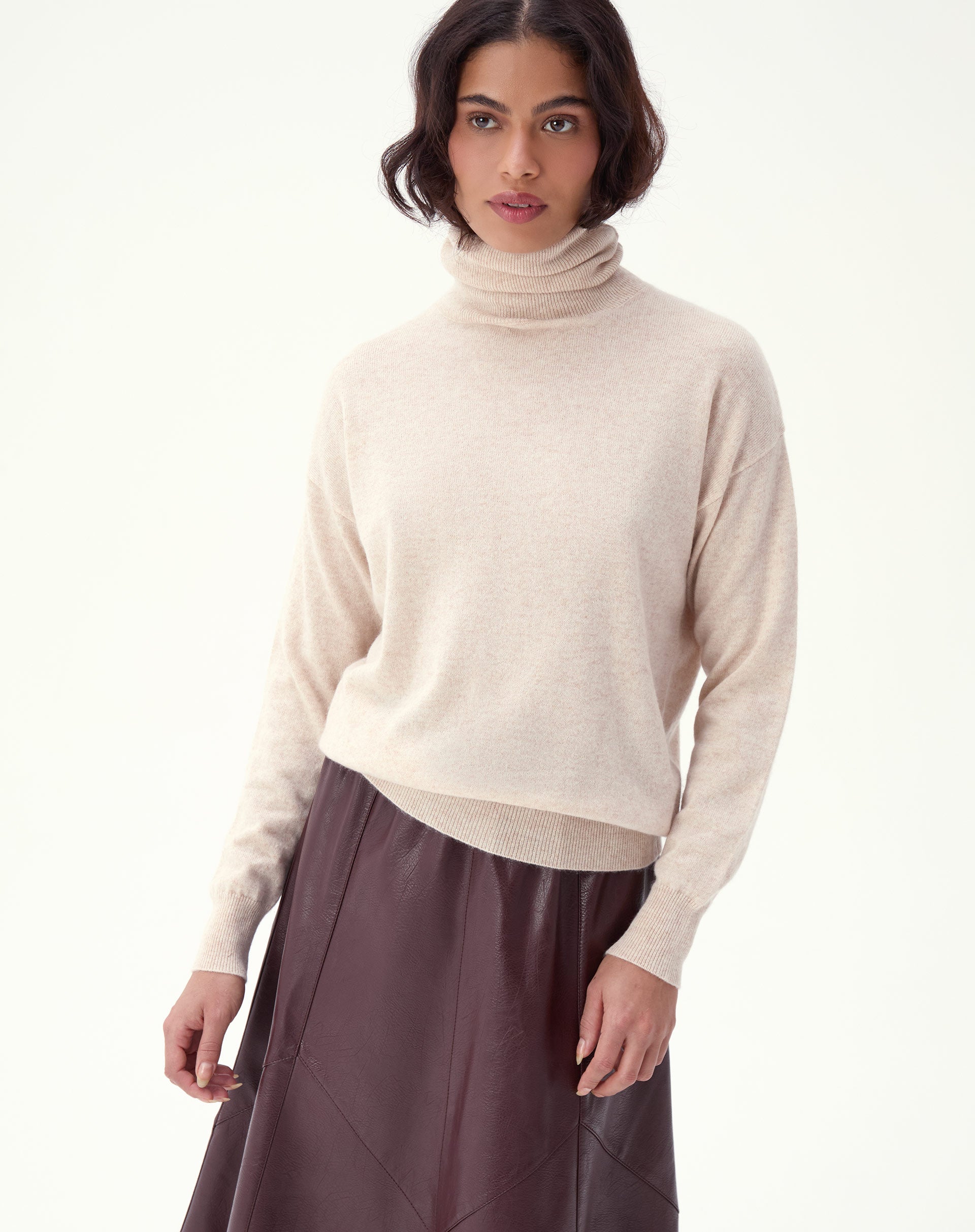 Modelo usando suéter cashmere areia em look com saia midi de couro, visão 3/4 frontal