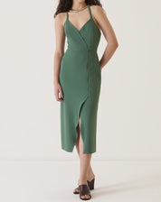 Modelo vestindo vestido verde com fenda frontal, alças finas e comprimento midi.