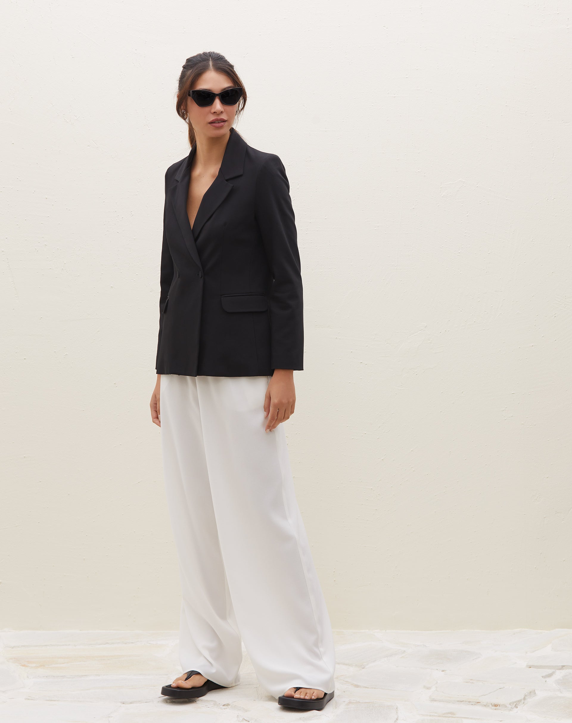 Blazer preto com lapela entalhada e bolsos com aba, combinado com calça branca.