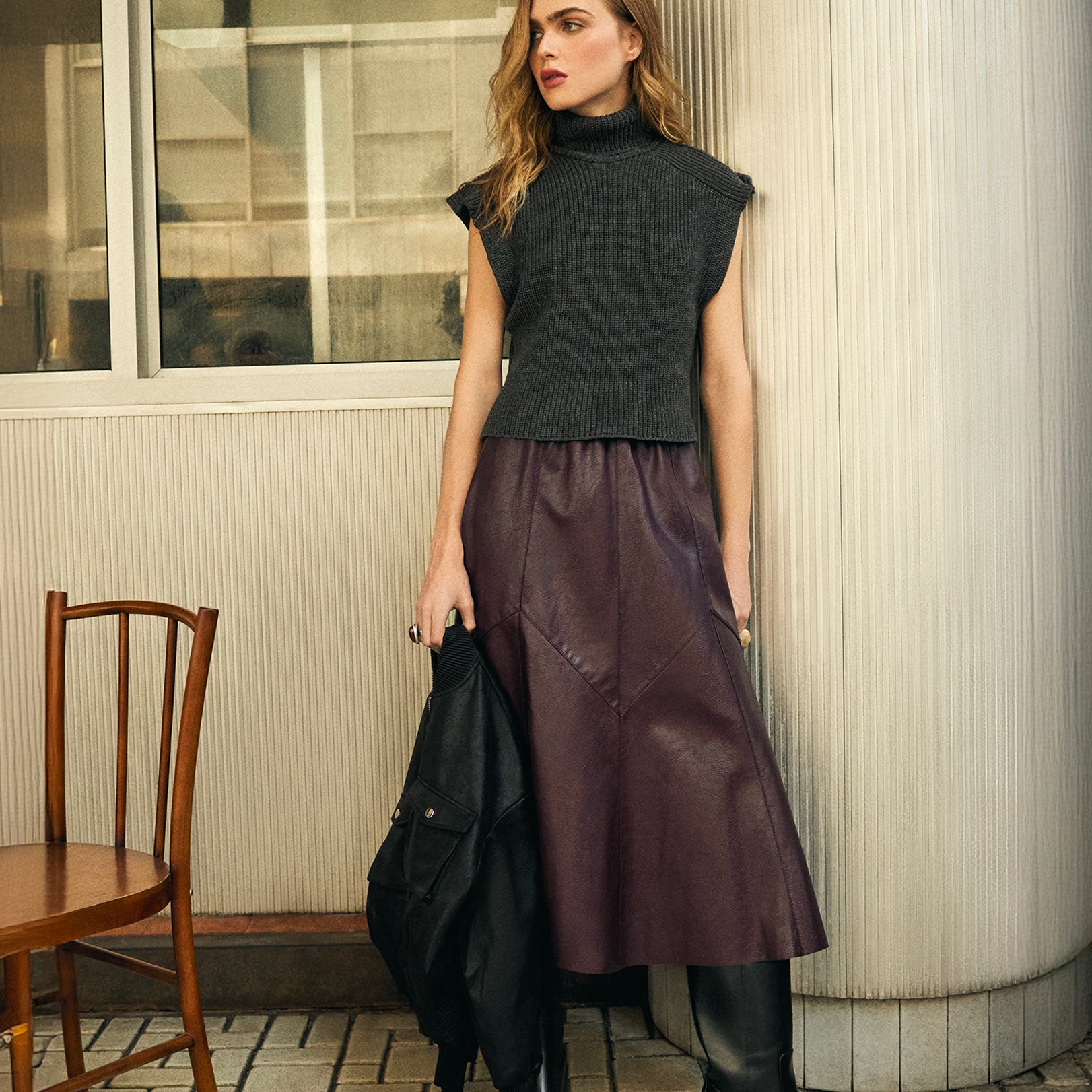 Saia midi burgundy em poliuretano com recortes assimétricos, vista em look urbano com top preto sem mangas e botas pretas - visual statement