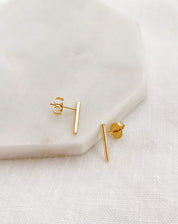 Brincos pequenos em formato de tubinho com acabamento liso e banho de ouro 18k sobre uma superfície branca.