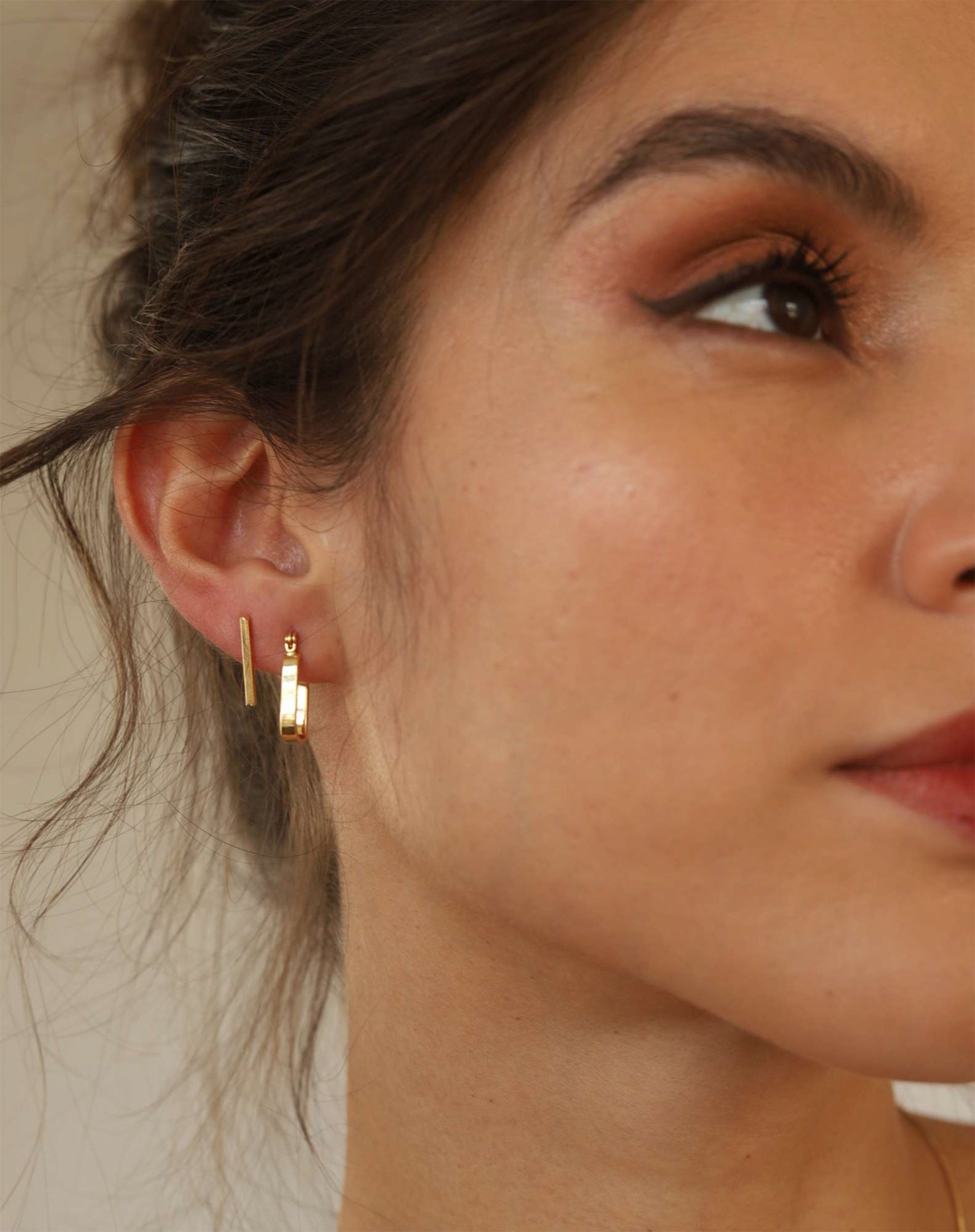 Brincos pequenos em formato de tubinho com acabamento liso e banho de ouro 18k usados no segundo furo da orelha.