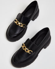 Mocassim Chunky preto com corrente de metal, vista frontal destacando o bico quadrado.