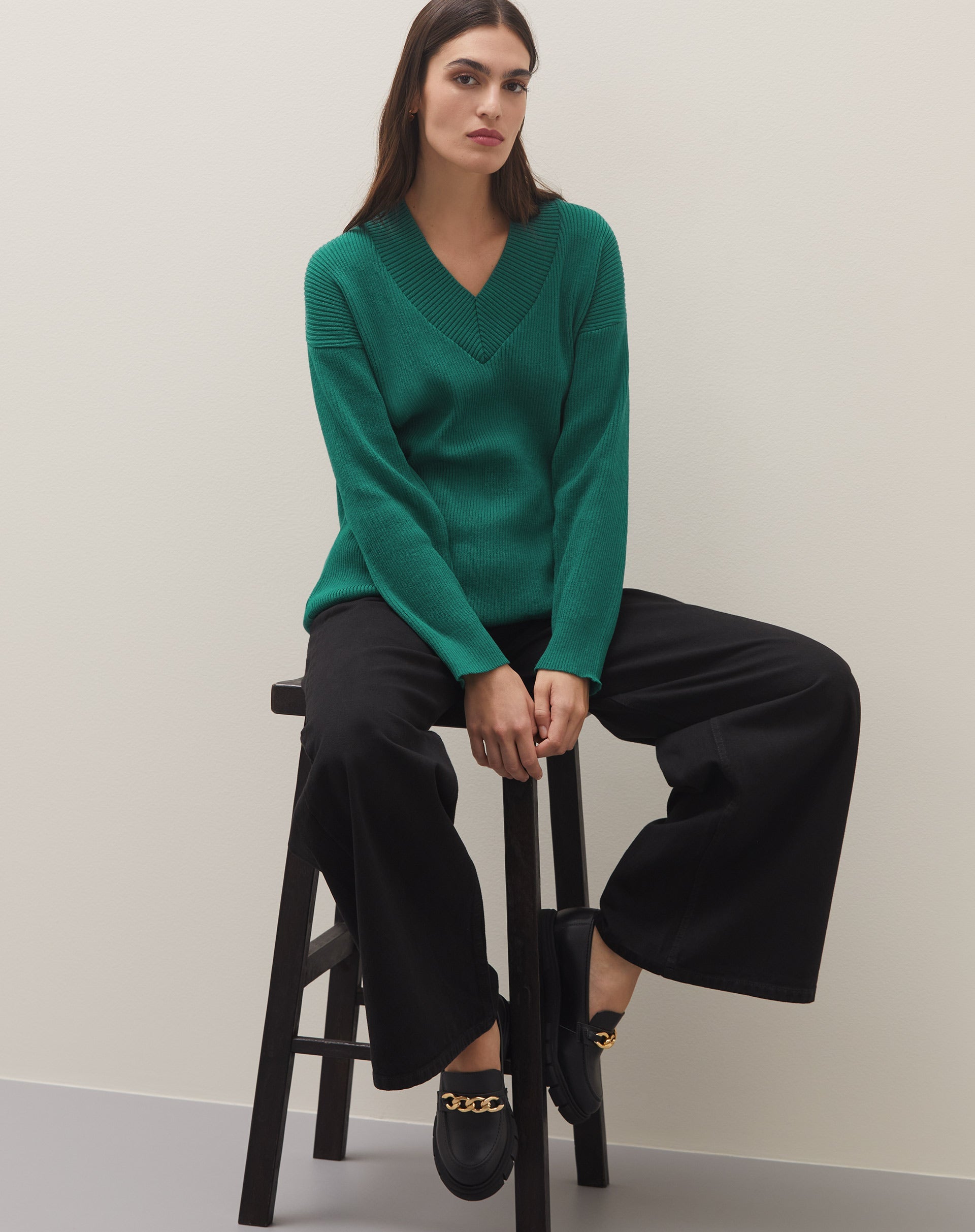 Modelo vestindo mocassim Chunky preto com corrente de metal, combinado com calça preta e blusa verde.