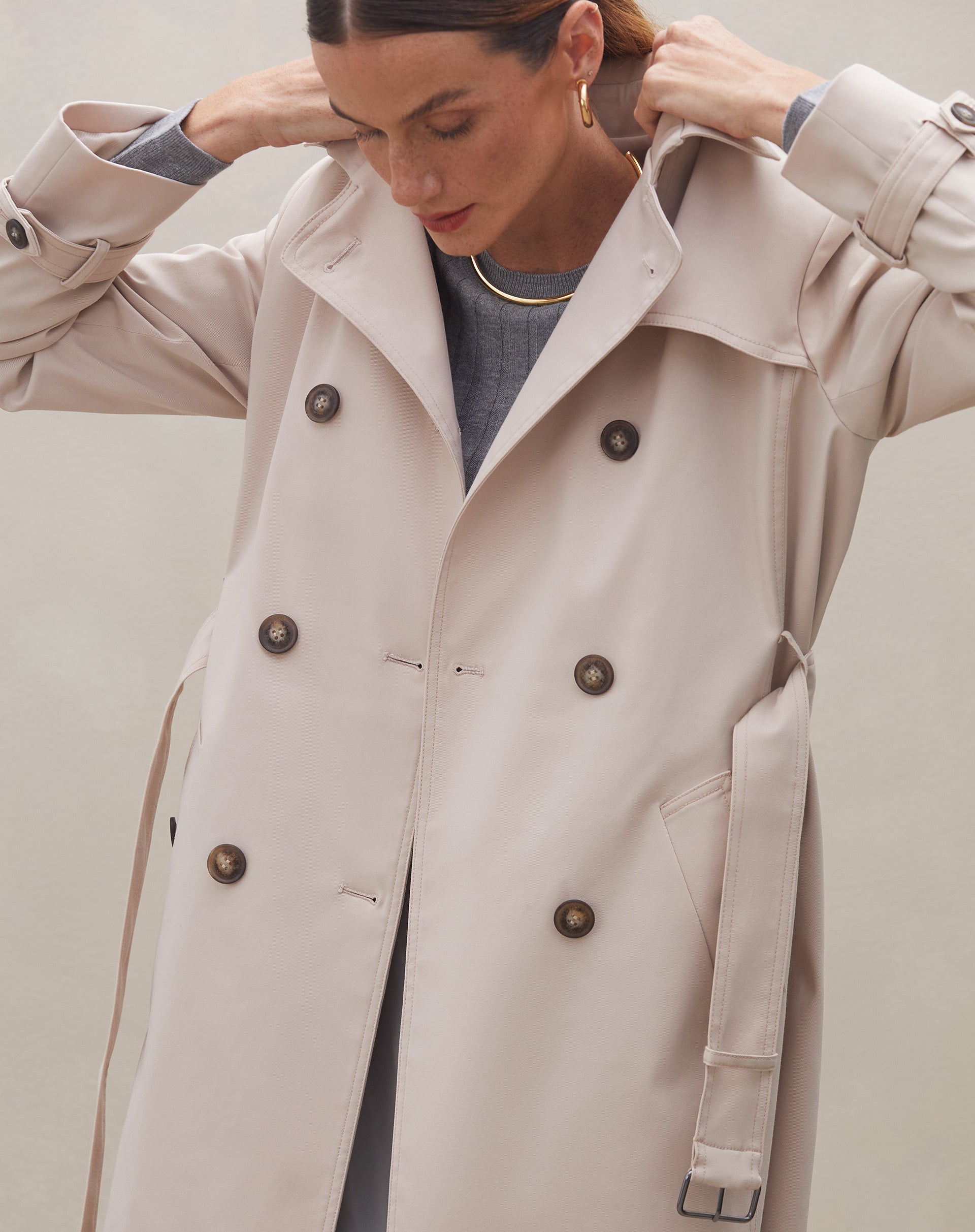 Detalhe do trench coat bege mostrando os botões e o cinto ajustável.