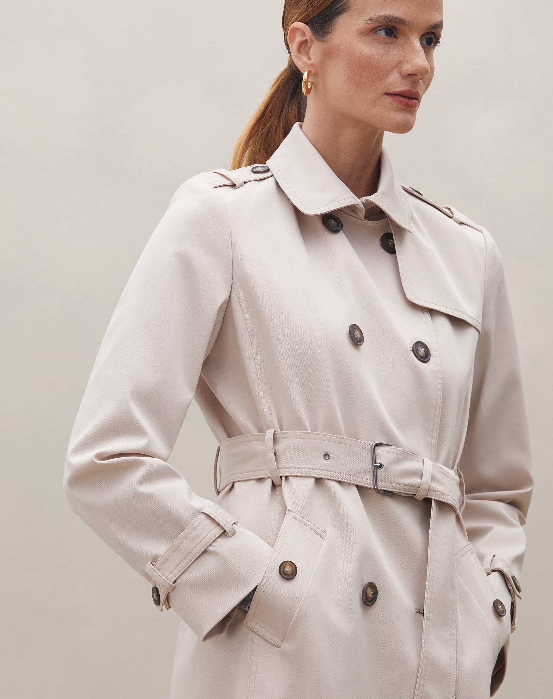 Modelo mostrando o lado do trench coat bege com detalhes do cinto.