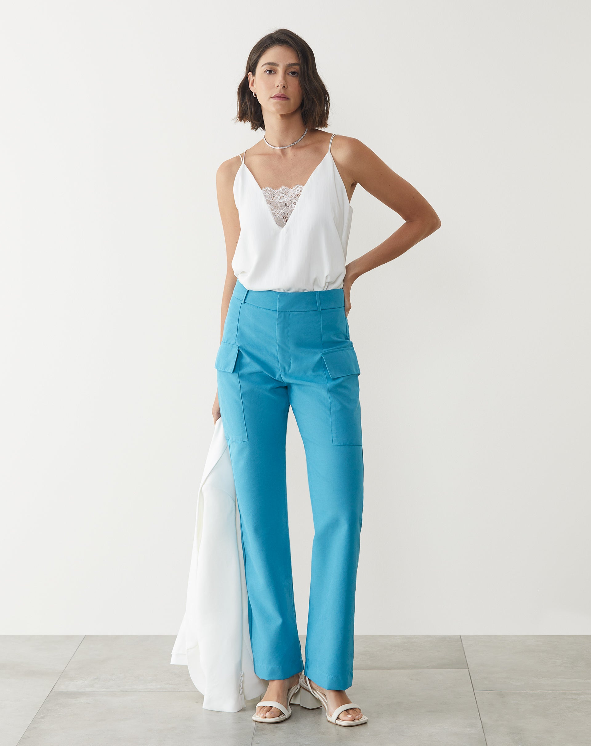 Modelo vestindo calça azul claro com blusa branca de alças finas.