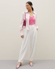 Camisa básica curta em rosa claro, combinada com calça branca e acessórios.