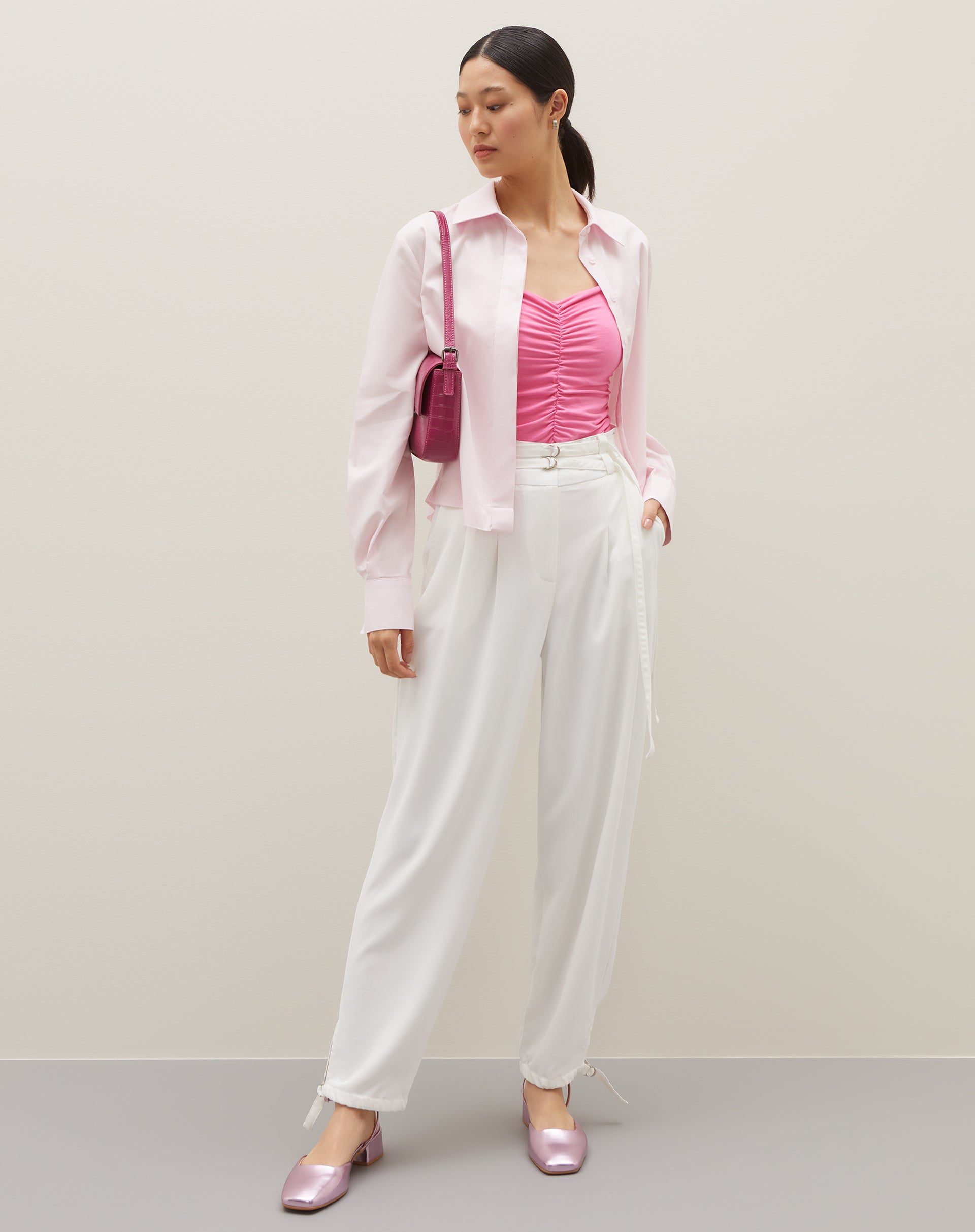 Camisa básica curta em rosa claro, combinada com calça branca e acessórios.