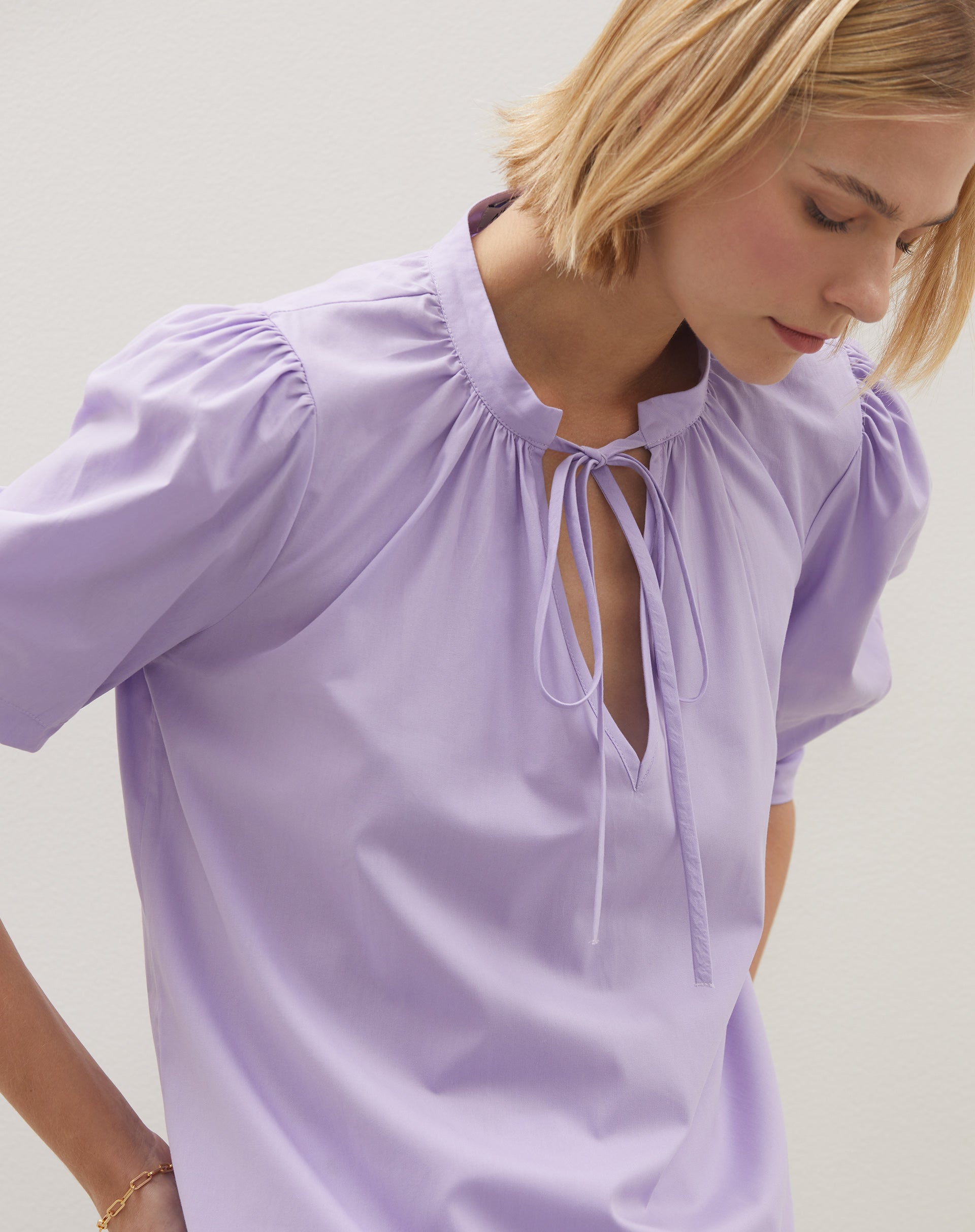 Detalhe do decote em V profundo da blusa lilás.
