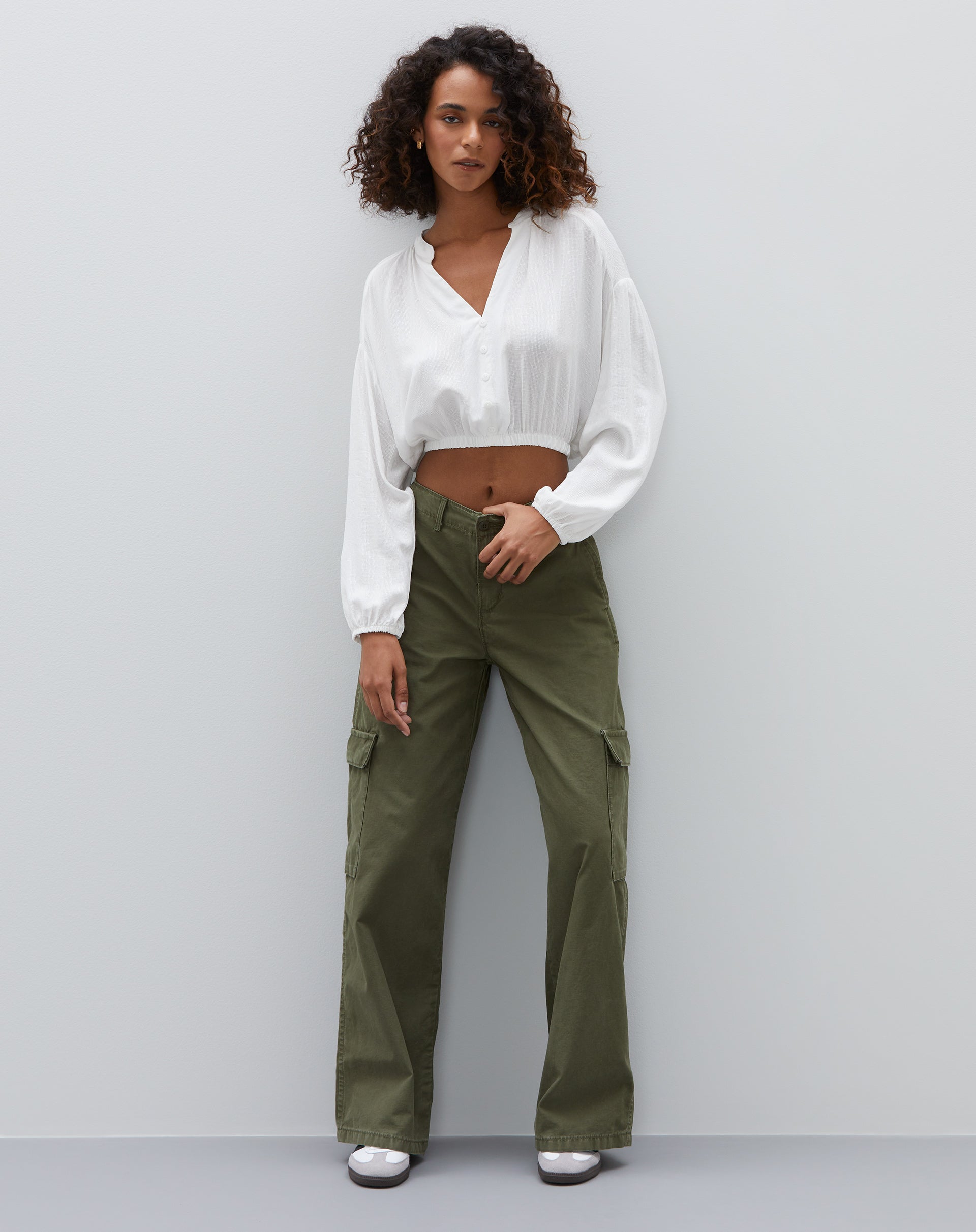 Modelo vestindo camisa cropped off-white com calça verde, vista completa.