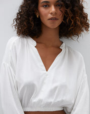 Detalhe do decote em V e fechamento com botões da camisa cropped off-white.