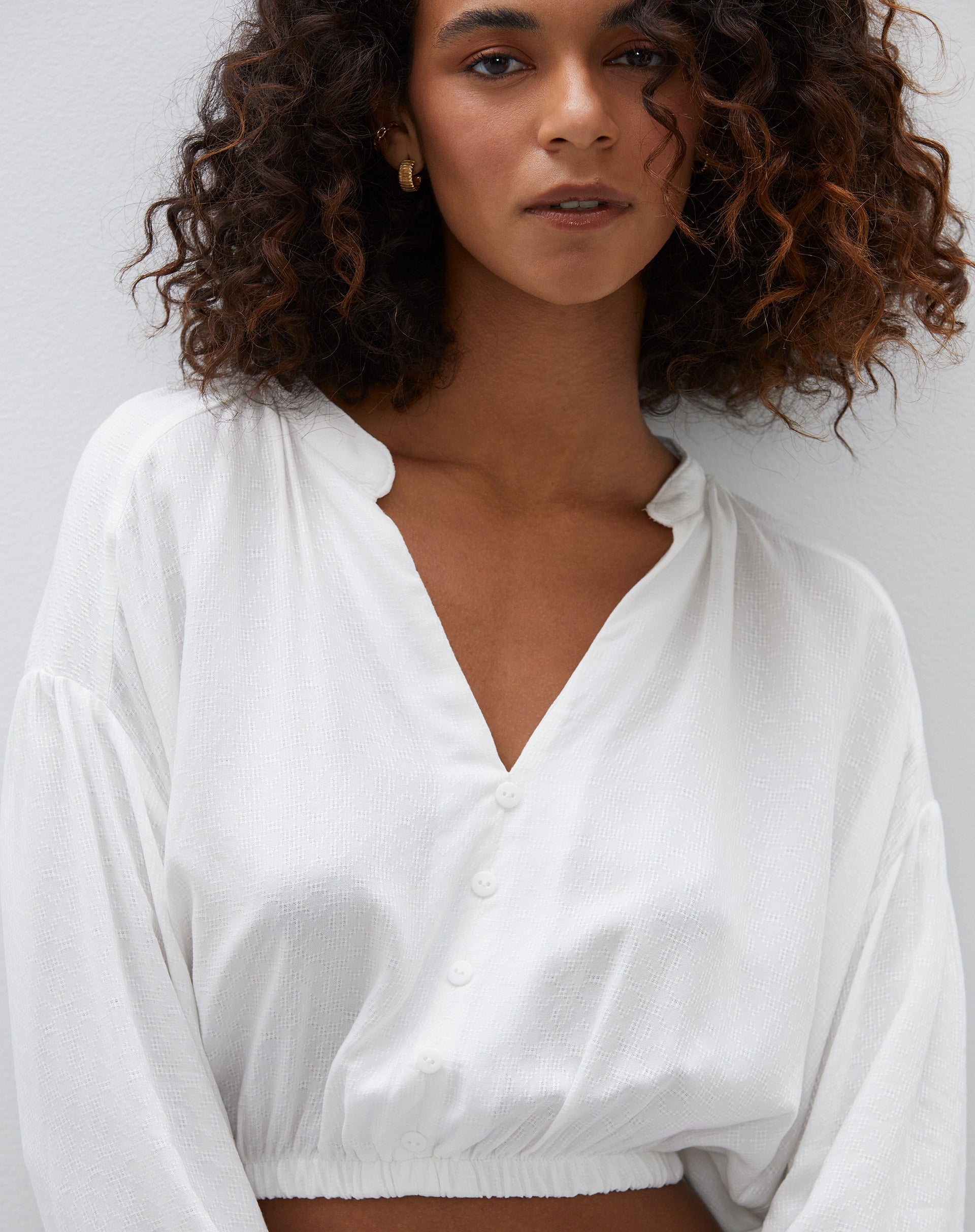 Detalhe do decote em V e fechamento com botões da camisa cropped off-white.
