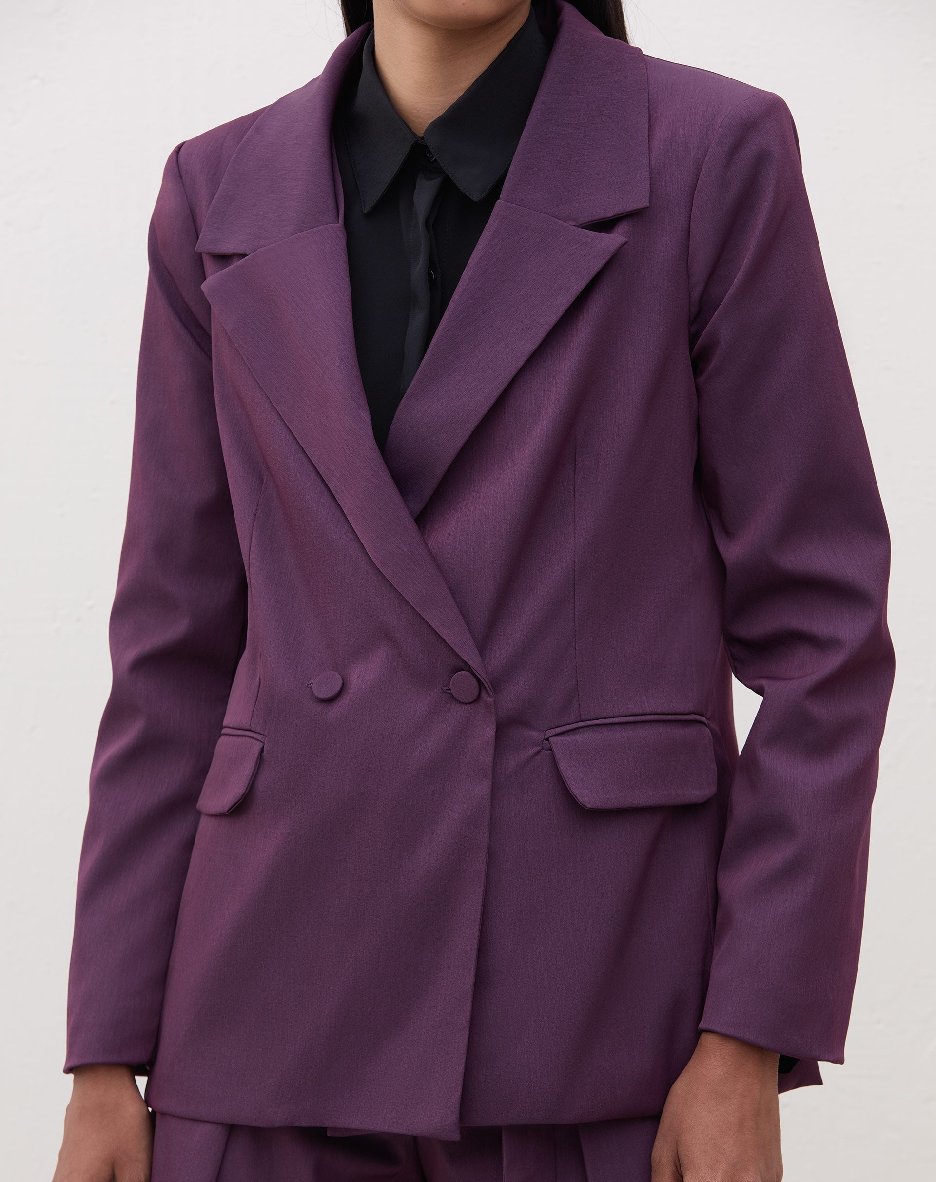 Detalhe do blazer roxo com lapelas entalhadas e fechamento transpassado.