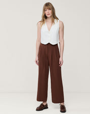 Modelo em estúdio usando calça reta cropped marrom com pregas vista frontal, cós com meia-elástico e bolsos laterais