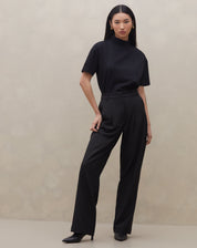 Modelo vestindo calça wide leg preta com pregas, vista frontal completa.