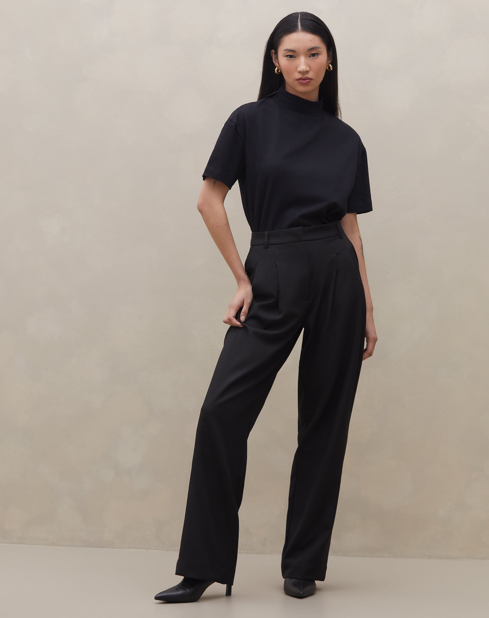 Modelo vestindo calça wide leg preta com pregas, vista frontal completa.