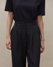 Detalhe da cintura alta e pregas da calça wide leg preta.