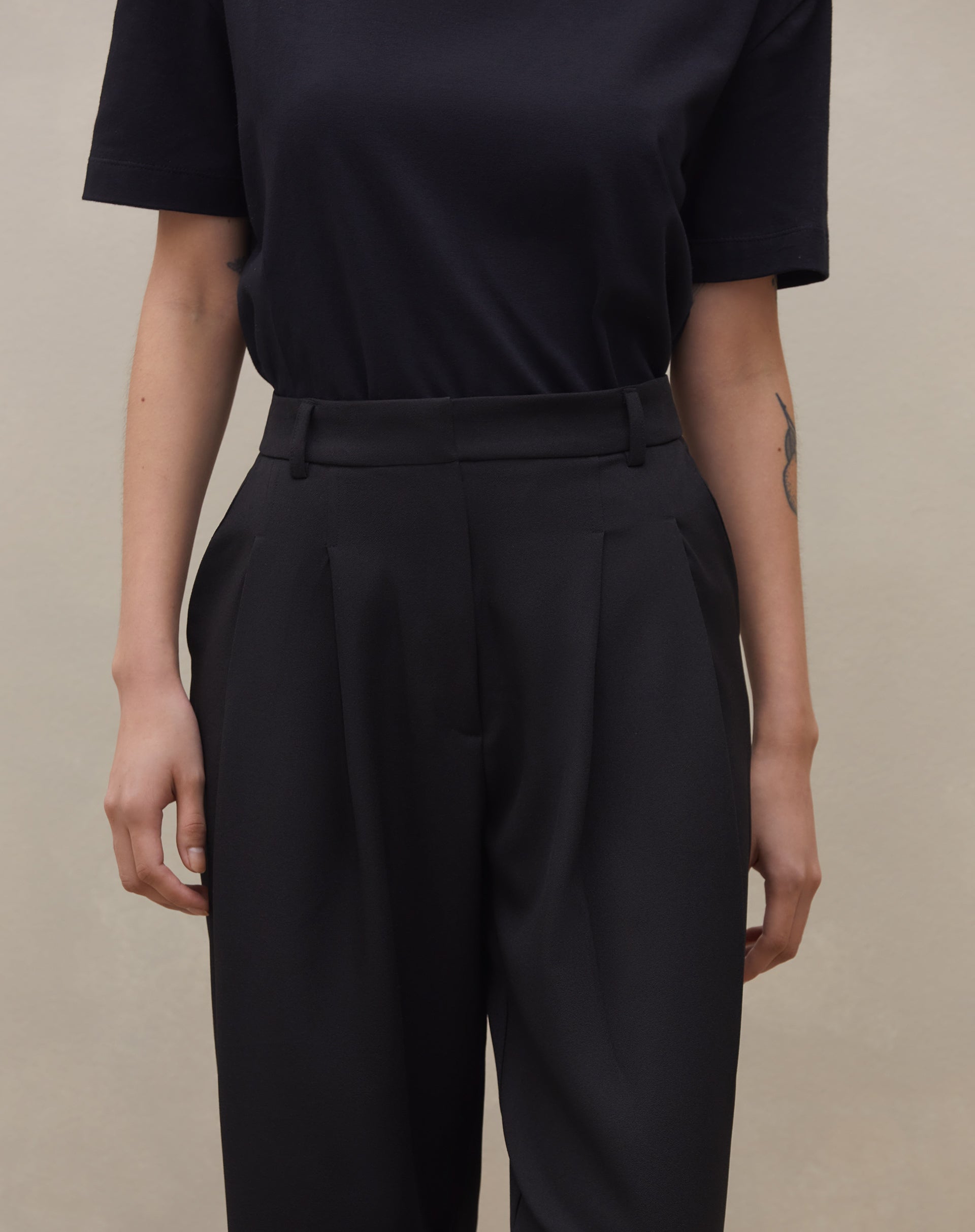 Detalhe da cintura alta e pregas da calça wide leg preta.