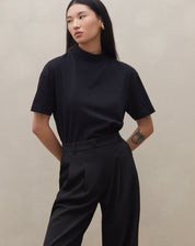 Modelo vestindo calça wide leg preta com pregas, vista traseira completa.