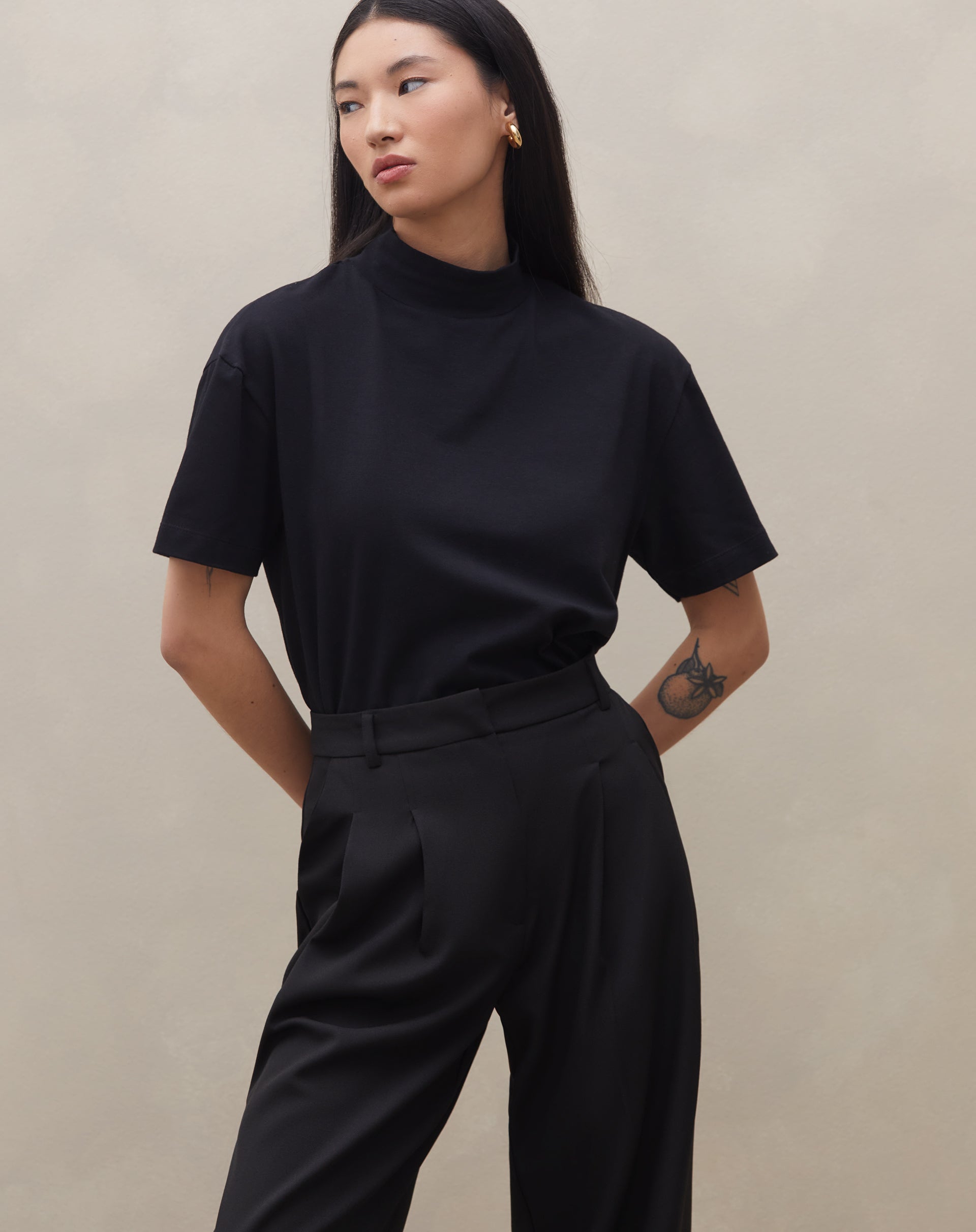 Modelo vestindo calça wide leg preta com pregas, vista traseira completa.