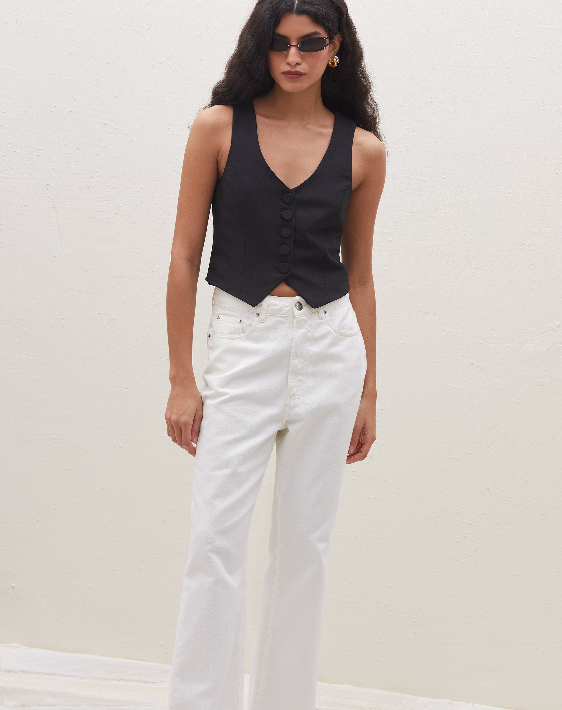 Modelo vestindo colete preto de alfaiataria com botões forrados e calça branca.