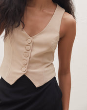 Imagem detalhada do colete de alfaiataria bege com botões forrados, mostrando o decote V.